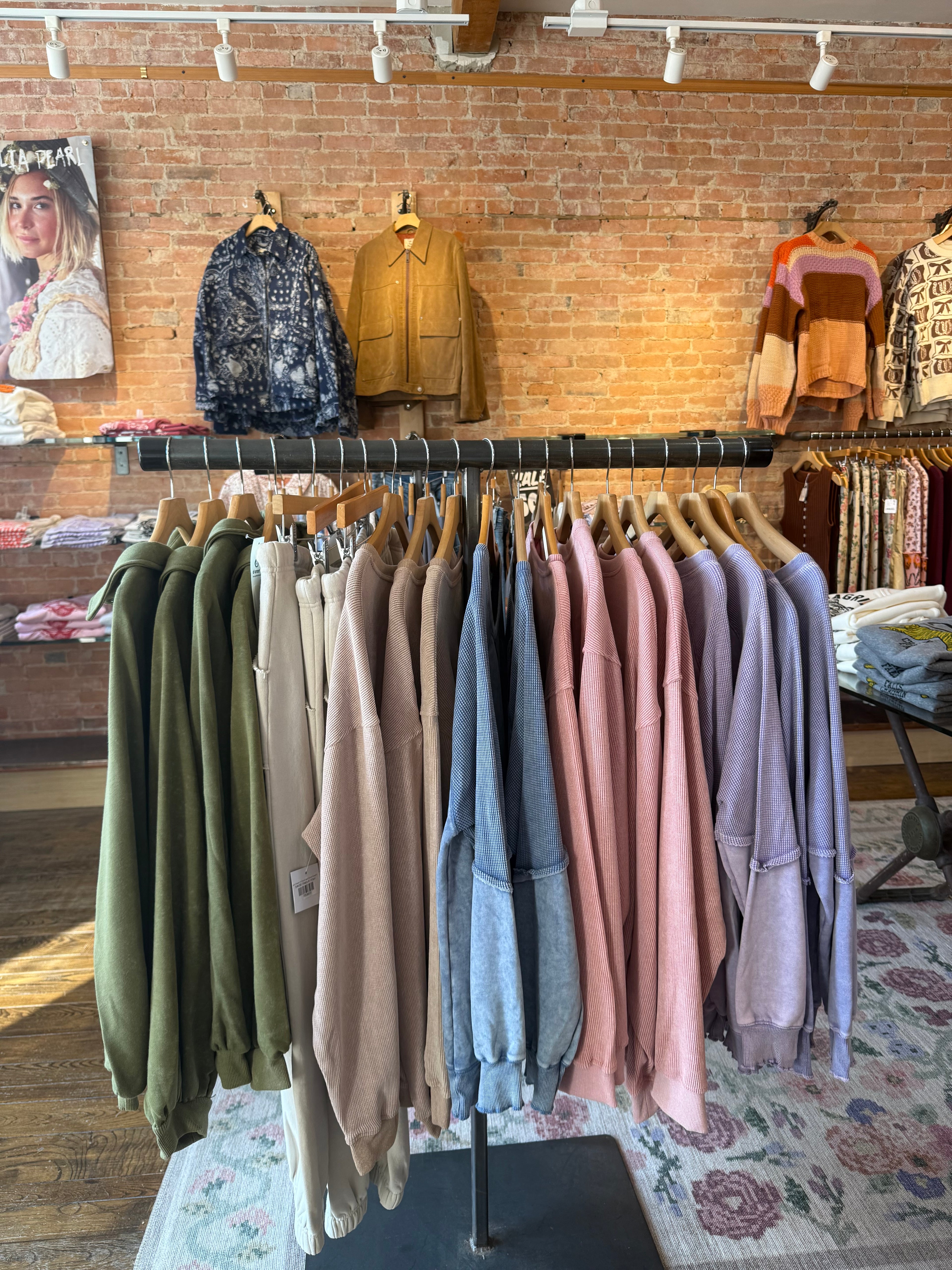 Row of folded shirts on a table with a patterned rug and brick wall in the background